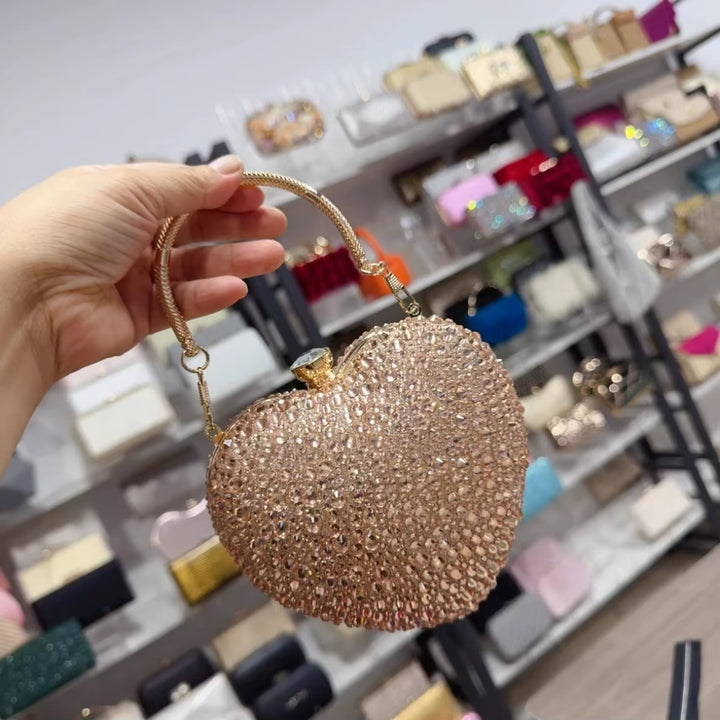 Visão frontal da Bolsa de festa clutch Feminina Champagne em formato de coração, cravejada com cristais azuis vibrantes, alça metálica dourada estruturada e fecho superior com detalhe em pedra – loja Bolsa Clutch