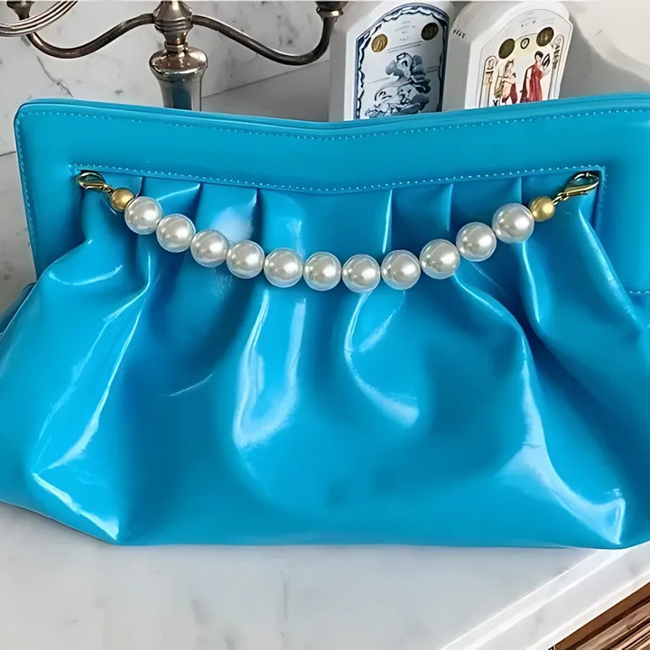 Detalhes das perolas da Bolsa clutch festa azul vibrante, em material sintético com efeito brilhante e drapeado. Detalhe frontal com alça de pérolas grandes douradas. Inclui alça dourada removível. Perfeita para eventos noturnos e ocasiões especiais.