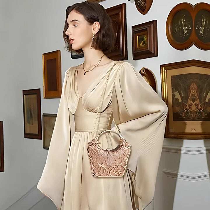 Mulher usando a Bolsa clutch festa dourada com acabamento metálico rendado, alça rígida escultural e aplicação de flores em strass, design exuberante e sofisticado – loja Bolsa Clutch