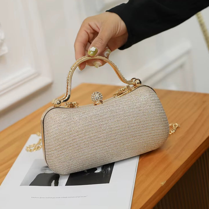 Imagem da Bolsa de mão clutch feminina festa dourada elegance com brilho, design retangular arredondado. Alça de mão superior dourada com strass, fecho de esfera cravejada e alça de corrente fina. Perfeita para eventos especiais e festas.