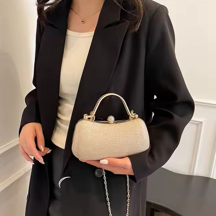 Mulher com a sua Bolsa de mão clutch festa dourada elegance com brilho, design retangular arredondado. Alça de mão superior dourada com strass, fecho de esfera cravejada e alça de corrente fina. Perfeita para eventos especiais e festas.