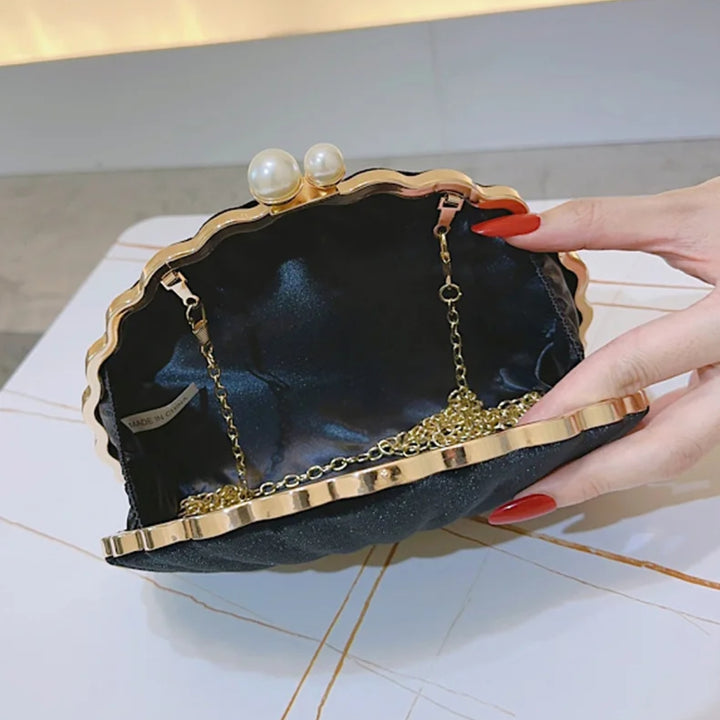 interior espaçoso e forrado da Bolsa clutch festa preta concha luxuosa, em veludo, com formato de concha e bordas douradas onduladas. Fecho superior com duas pérolas e alça de corrente fina dourada. Ideal para casamentos, formaturas e eventos elegantes.