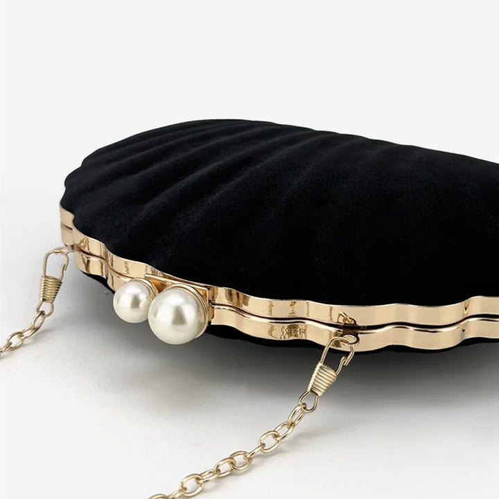 Detalhes do fecho da Bolsa clutch festa preta concha luxuosa, em veludo, com formato de concha e bordas douradas onduladas. Fecho superior com duas pérolas e alça de corrente fina dourada. Ideal para casamentos, formaturas e eventos elegantes.