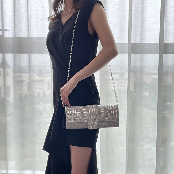 Mulher usando com a alça lateral sua linda Bolsa clutch festa prata retangular com acabamento em strass tipo diamante, design estruturado com aba frontal e fecho magnético elegante – loja Bolsa Clutch