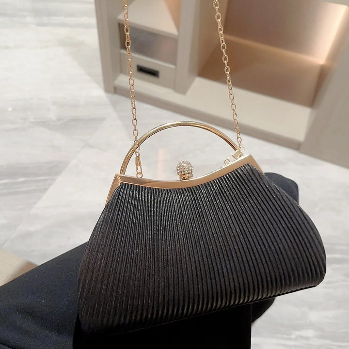 Detalhes da Bolsa clutch festa preta com tecido plissado e brilho sutil, alça metálica dourada, fecho com detalhe de joia e corrente delicada para usar no ombro – loja Bolsa Clutch