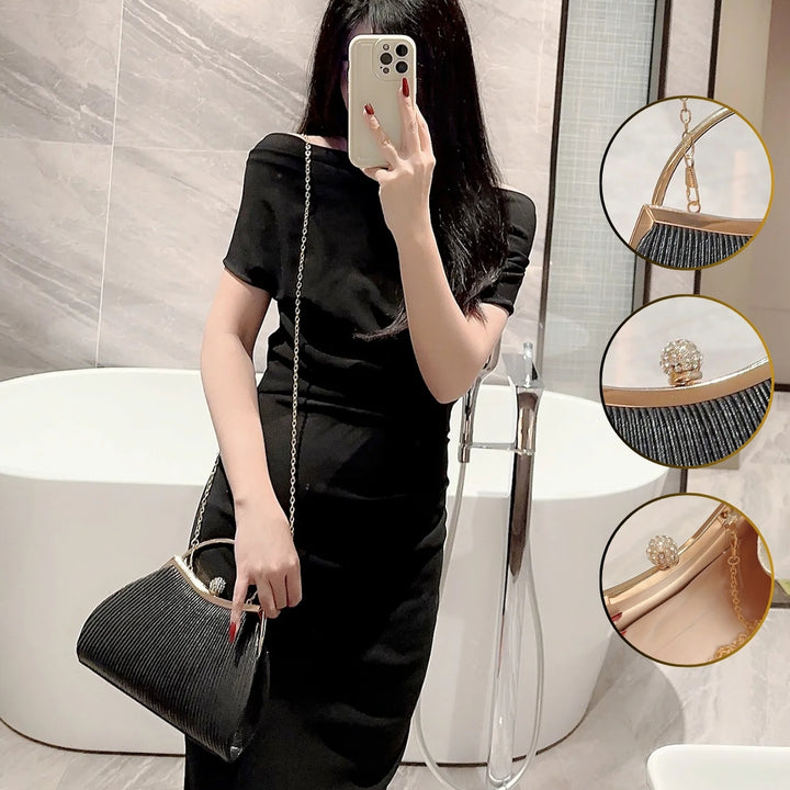Mulher em ambiente chique com a Bolsa clutch festa preta com tecido plissado e brilho sutil, alça metálica dourada, fecho com detalhe de joia e corrente delicada para usar no ombro – loja Bolsa Clutch