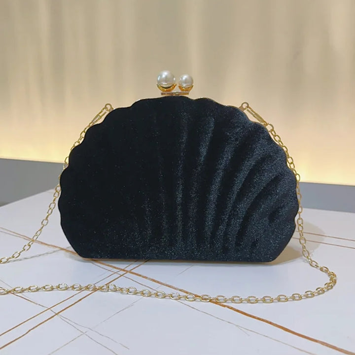 Bolsa de mão feminina clutch festa preta concha luxuosa, em veludo, com formato de concha e bordas douradas onduladas. Fecho superior com duas pérolas e alça de corrente fina dourada. Ideal para casamentos, formaturas e eventos elegantes.