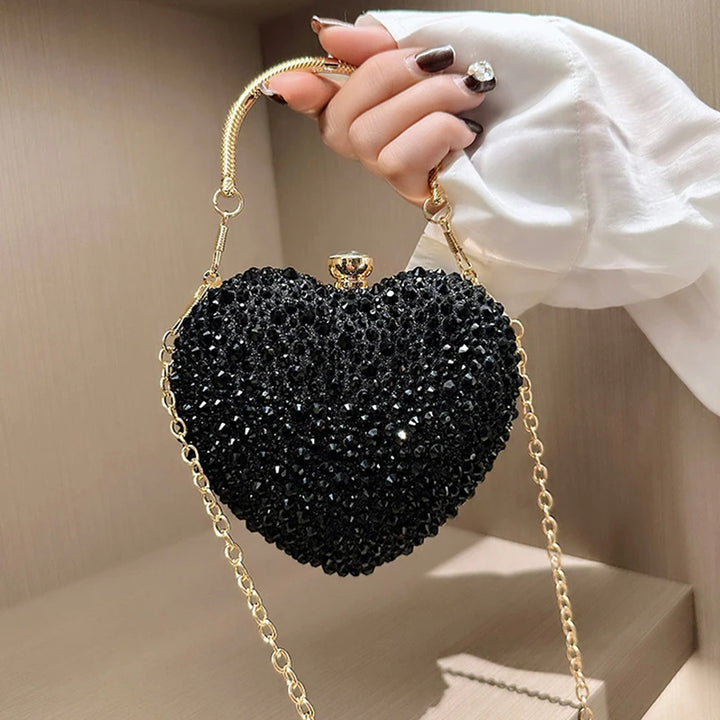 Mão com a Bolsa de festa clutch Feminina Preta em formato de coração, cravejada com cristais azuis vibrantes, alça metálica dourada estruturada e fecho superior com detalhe em pedra – loja Bolsa Clutch Bolsa-Clutch-Festa-Preta-Coração-bolsa-pequena-de-festa--loja-bolsa-clutch-0002