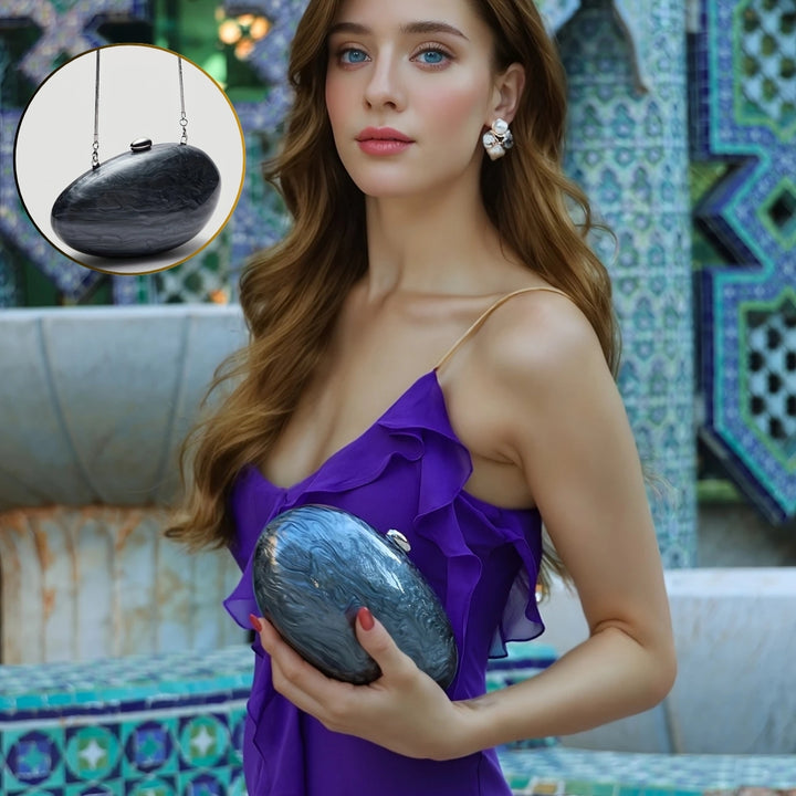 Mulher de vestido roxo e olhos claros segurando na altura do peito Clutch preta oval com acabamento perolado luxuoso e corrente dourada, perfeita para festas, casamentos ou eventos de gala – loja Bolsa Clutch.