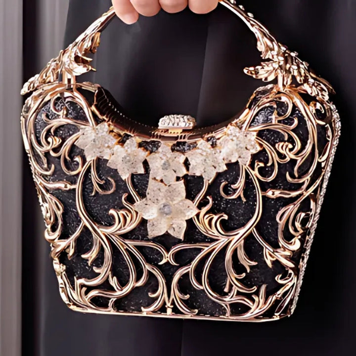 Bolsa de mão feminina clutch festa preta com acabamento metálico dourado rendado, alça rígida escultural e aplicação de flores em strass, design exuberante e sofisticado – loja Bolsa Clutch