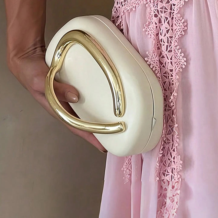Mulher de vestido rosa segurando a Bolsa clutch festa branca e dourada. Design moderno com alça de mão dourada curva integrada e alça de corrente. Ideal para eventos.