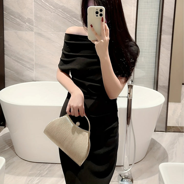 Mulher segurando a Bolsa clutch festa prata com brilho dourado, tecido plissado elegante, alça metálica prateada estruturada, fecho com detalhe de joia e corrente fina removível – loja Bolsa Clutch