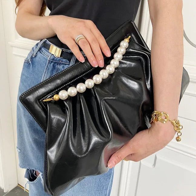 Modelo com a Bolsa clutch festa preta pérolas, linda e elegante, em material sintético com efeito drapeado. Possui alça superior fixa de pérolas brancas com terminais dourados. Tamanho médio, inclui bolso interno com zíper. Ideal para festas e eventos.